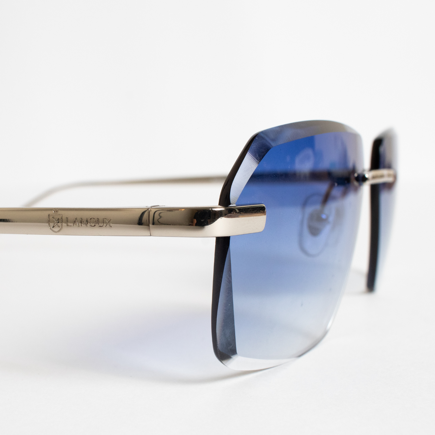 The 'Sancy' model sunglasses, capturing the elegance of rimless onyx blue gradient lenses set in 18k gold frames with a diamond cut. This side view highlights the fine detailing and craftsmanship, with the brand's emblem subtly engraved on the gold temple against a crisp white background.