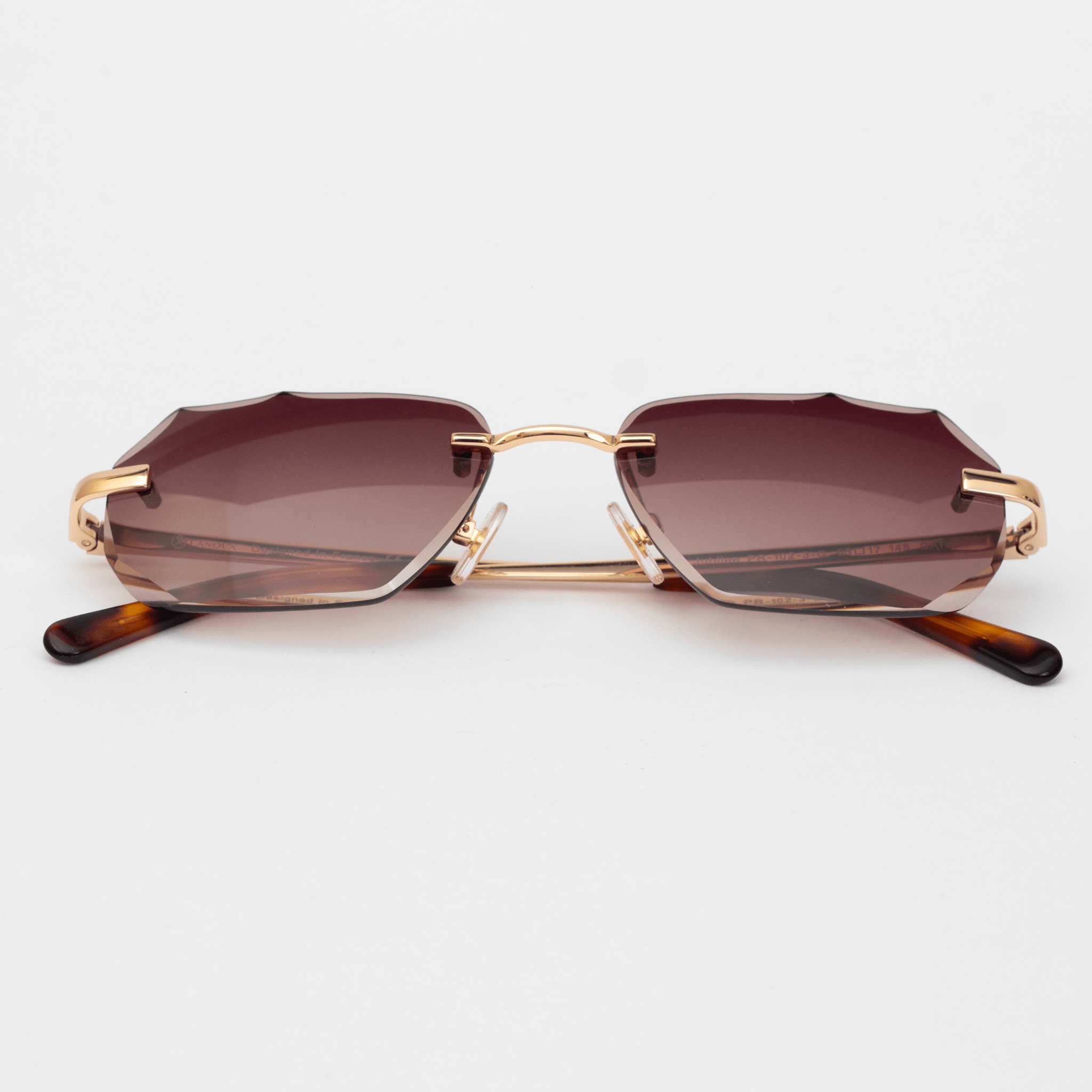Elegant rimless sunglasses featuring a unique diamond-cut lens design, with 18k gold-plated hardware. The arms display a tortoiseshell pattern, complementing the brown gradient of the diamond-cut lenses.