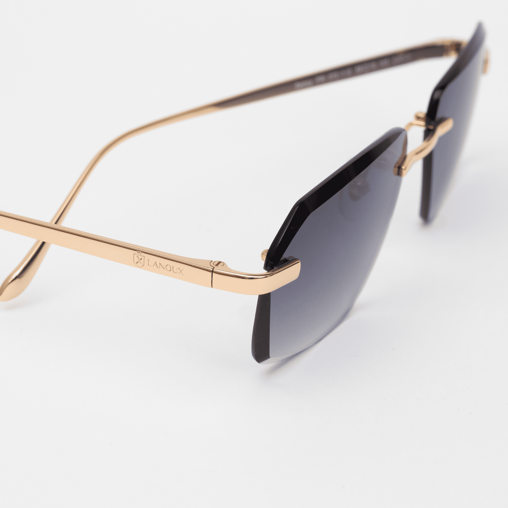 Close-up view of the Model Sancy sunglasses showing the detailed craftsmanship of the rose gold temple with the 'LANOUX' logo and the grey diamond-cut rimless lenses, set against a white surface.
