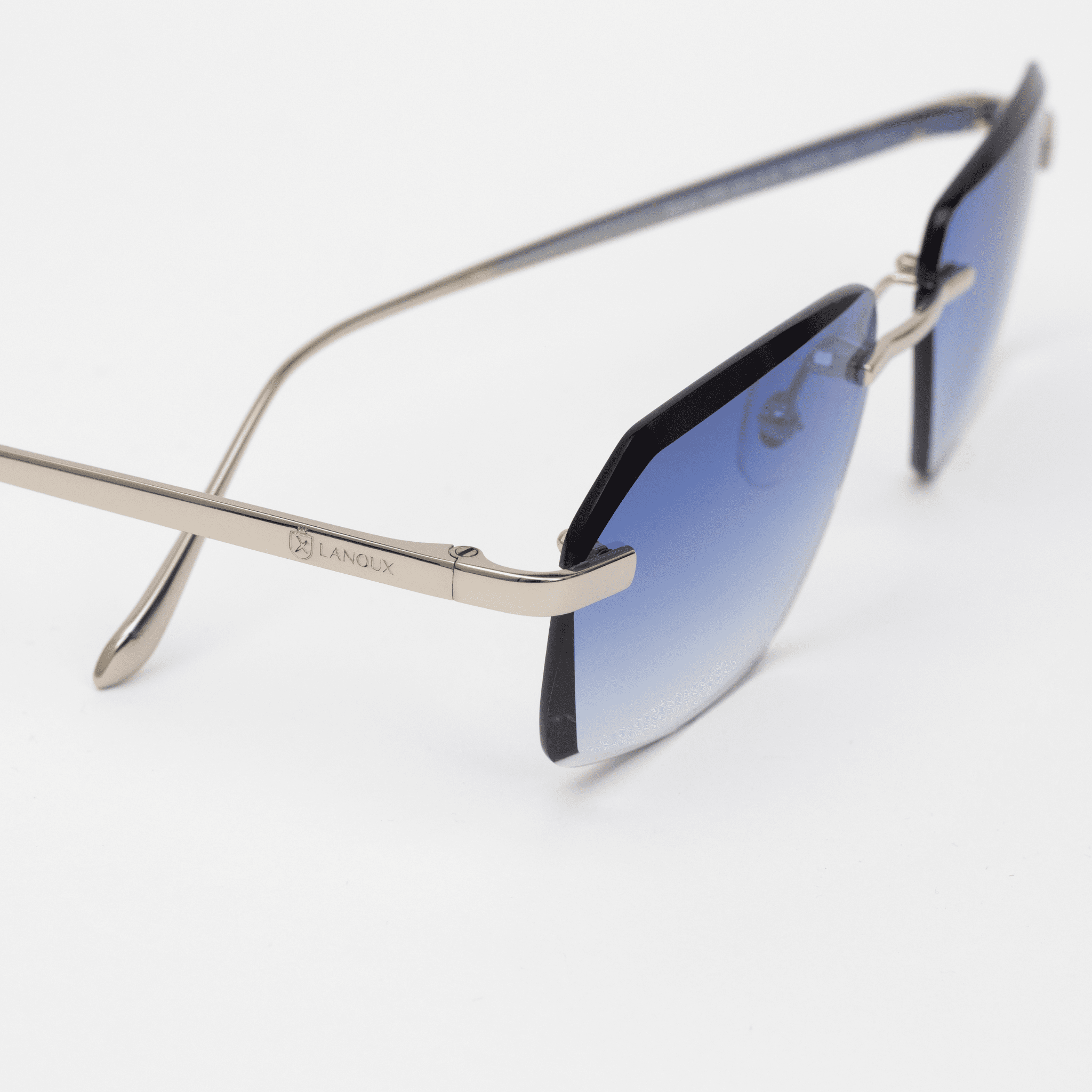 Close-up of the side of Sancy model sunglasses, displaying the elegant sterling silver arm with the 'LANOUX' logo, alongside the onyx blue diamond-cut rimless lenses, against a white background